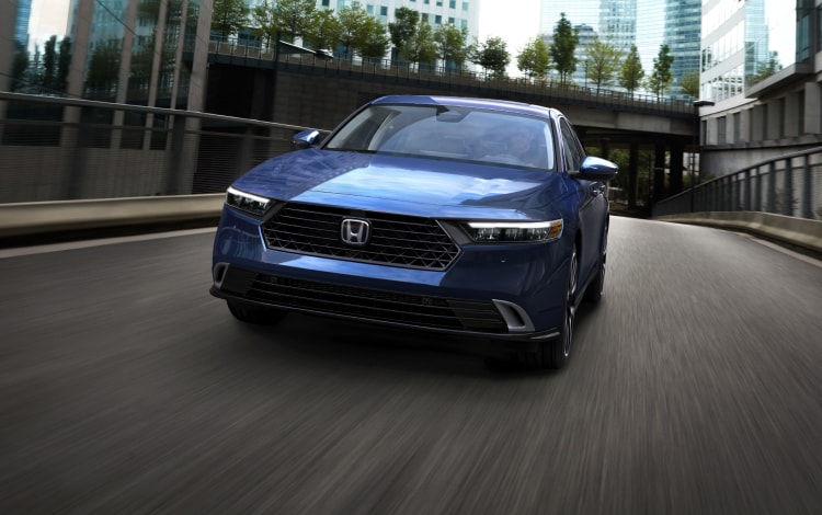 2024 Honda Accord Touring Hybrid in Canyon River Blue Metallic driving down a city street, showing the stylish grille and front end.
